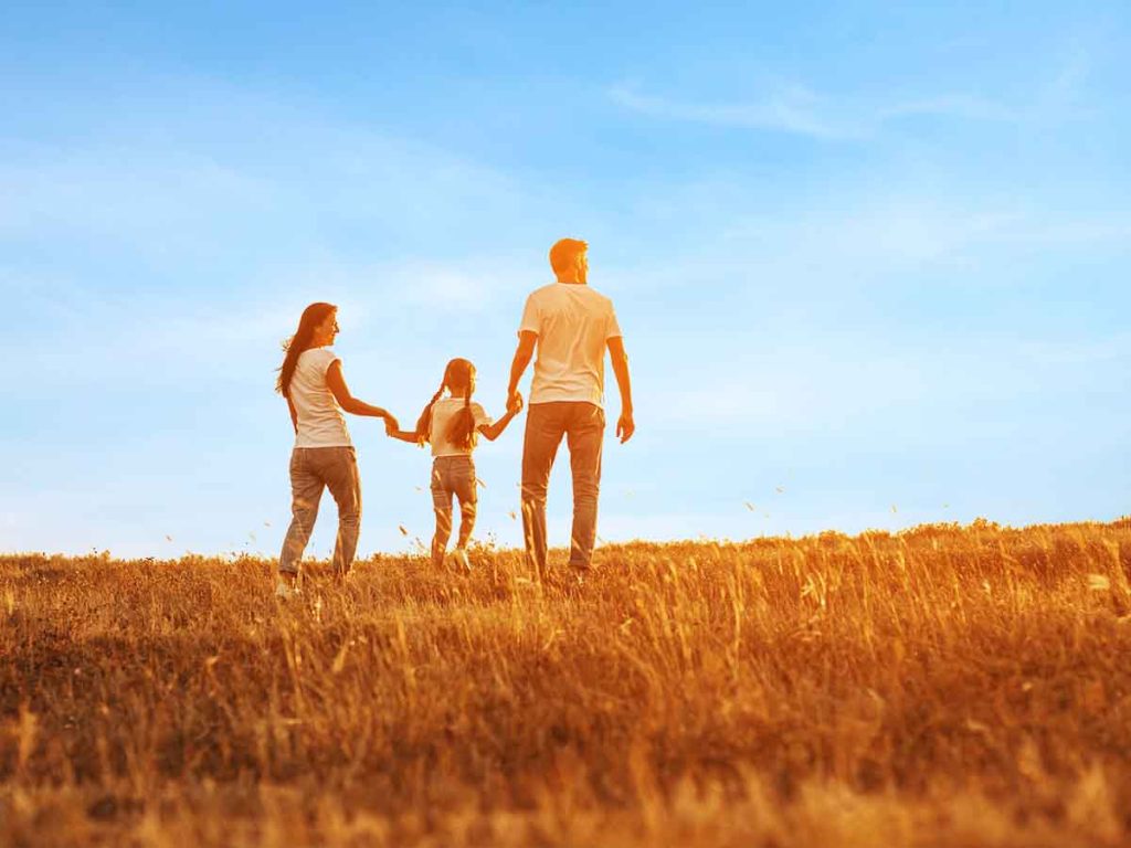 Comprehensive Care - Parents and young child in field with sun at their backs.
